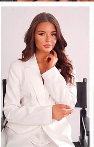 Jen K in a white tailored suit, seated studio portrait